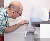 A Caucasian man and a washing machine. A man pours a portion of fabric softener.