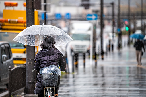 Kyoto, Japan - April 10, 2019: Gojo-dori street during rainy day and people woman riding bicycle bike holding umbrella on sidewalk