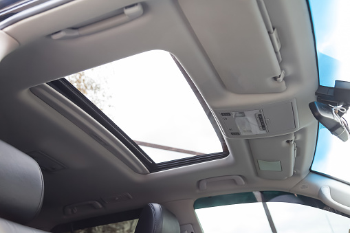 Vista del techo del coche con una escotilla de vidrio transparente para el aire, abriéndose en verano mientras se conduce rápido en la cabina gris del vehículo. Techo corredizo sobre techo beige de color claro. photo