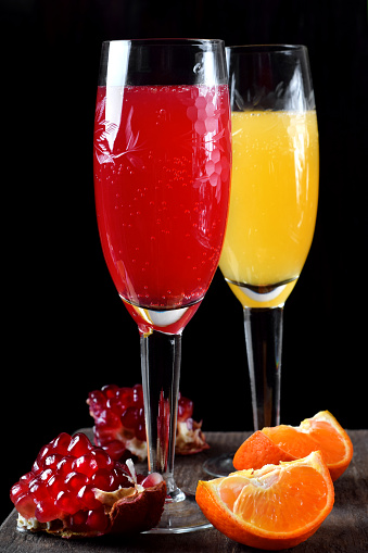 Red and yellow cocktails with champagne and fruit syrups in a champagne glass against the black background