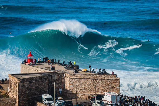 nazare, portugal, surfer riding huge wave near the fort of nazare lighthouse - sea water surf tide photos et images de collection