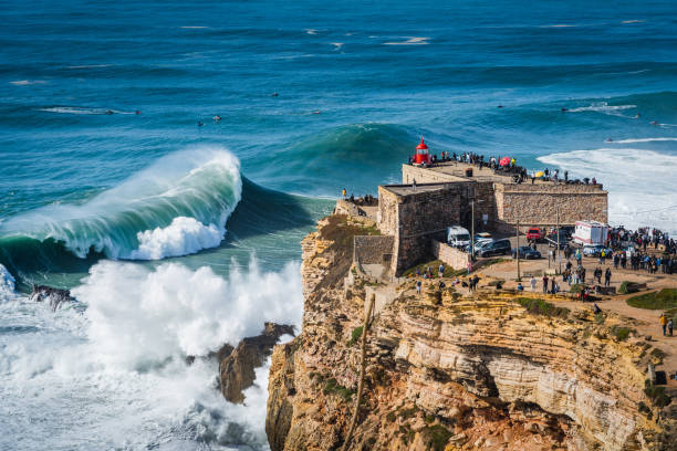 nazare, portugal, enormes olas rompiendo cerca del fuerte del faro de san miguel arcanjo - big wave surfing fotografías e imágenes de stock