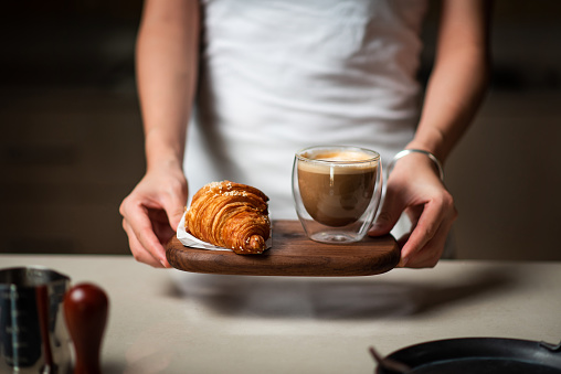 Female with a cup of coffee with croissant at home close up