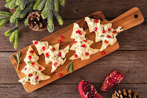 Christmas tree appetizers with feta, pomegranate and rosemary. Overhead on a serving board against wood.