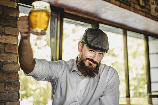 Happy bearded man who drinks beer in the pub - Young hipster man - Portrait of a young man with a beard holding a beer