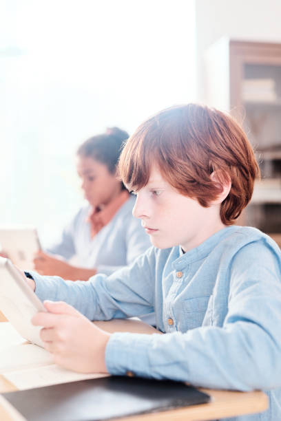 istock Serious clever schoolkid with tablet looking through text on display at lesson 1283210904