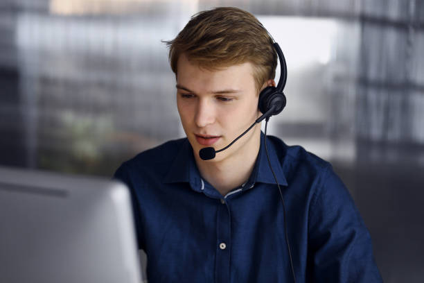 Young blond businessman using headset and computer at work. Startup business means working hard and out of time for success achievement Young blond businessman using headset and computer at work. Startup business means working hard and out of time for success achievement. only young men stock pictures, royalty-free photos & images