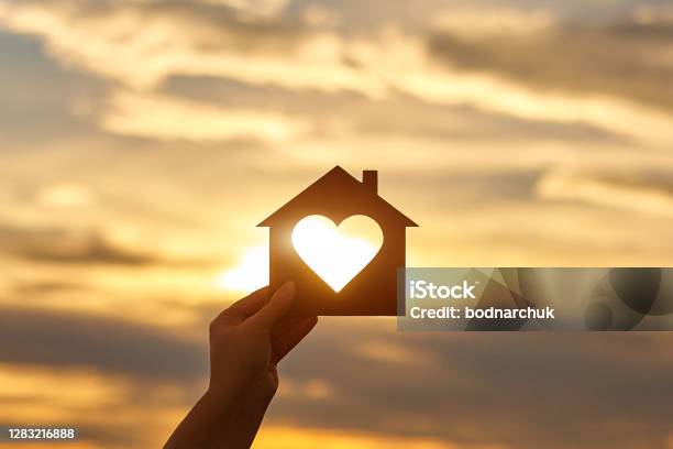Woman Hand Holds Wooden House In The Form Of Heart Against The Sun Stock Photo - Download Image Now