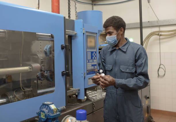 Young black worker is using heavy machinery at a factory with face mask. New normal. COVID-19 concepts.