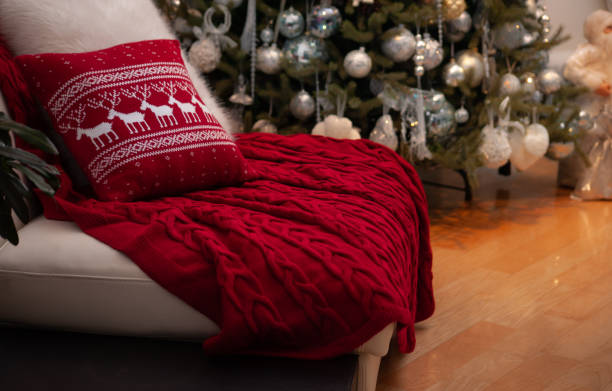 istock Christmas still life with gorgeous red knitted blanket and deers pattern cushion on a couch and decorated Christmas tree on the back 1283221502