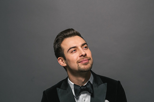 A handsome man in a suit with a bow tie is posing for a photo in the dark