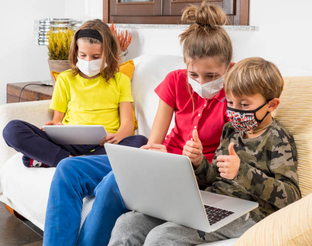 istock Children with masks coronavirus study in lockdown with laptop on the sofa at home, using the wi-fi network.
