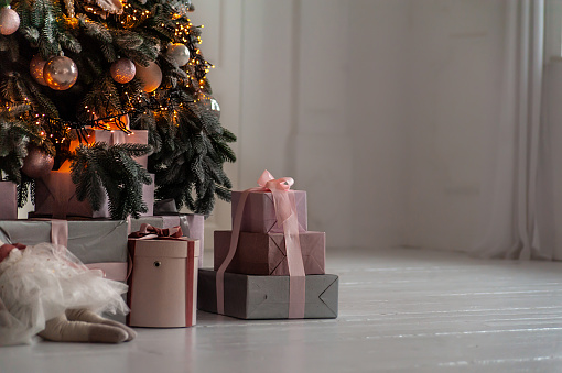 Gifts boxes under decorated Christmas tree in white room with white wooden floor
