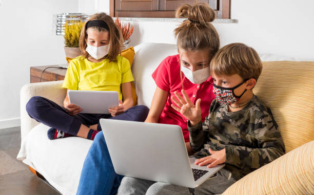istock Children with masks coronavirus study in lockdown with laptop on the sofa at home, using the wi-fi network.