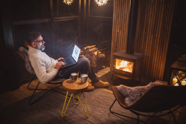 Cozy winter night Man enjoy in warm cozy fire near fireplace, he using laptop cottage life stock pictures, royalty-free photos & images