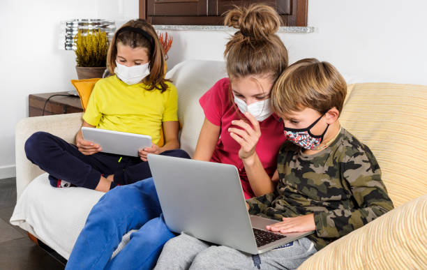istock Children with masks coronavirus study in lockdown with laptop on the sofa at home, using the wi-fi network.