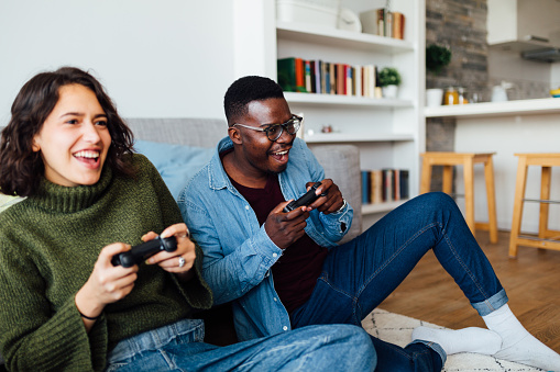 Happy smiling interracial couple having fun at home, relaxing and playing video games, enjoying themselves