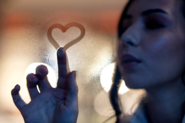 istock Young woman drawing on fogged-up windowpane 1283227361
