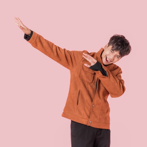 Portrait of asian handsome young man in fashionable clothing and enjoy standing with gesture dab dance Portrait of asian handsome young man in fashionable clothing and enjoy standing with gesture dab dance isolated on pink background. dab dance photos stock pictures, royalty-free photos & images