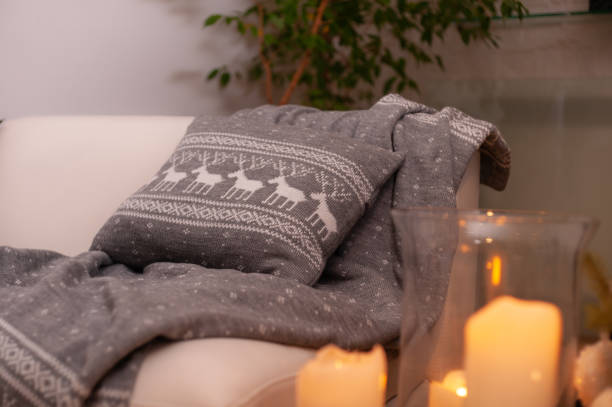 istock Christmas still life with grey knit blanket and cushion with deers pattern on a couch, big candles on a floor and decorated Christmas tree on the back 1283233009