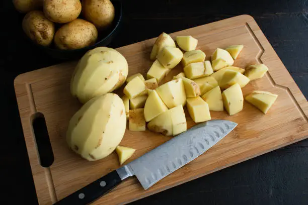 Chopping raw peeled potatoes on a bamboo cutting board