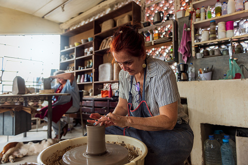 Mature woman artist making clay bowl on pottery wheel