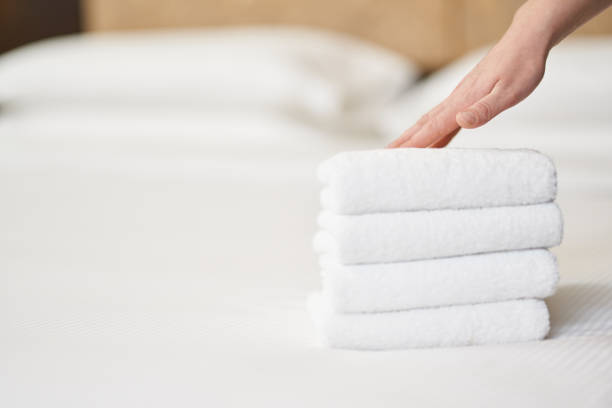 istock Female hand touching stack of fresh white bath towels on the bed 1283239573
