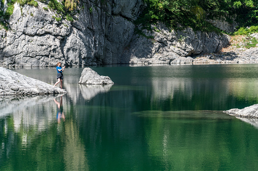 One Mature women standing at the Black Lake in Triglav National Park and taking selfie.