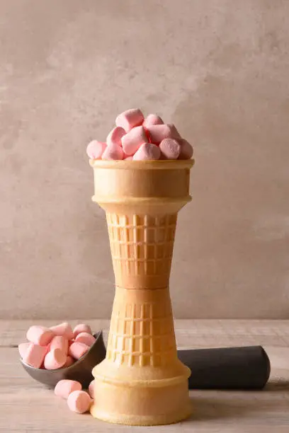 Stacked ice cream cones filled with pink marshmallows and a scoop in the background.