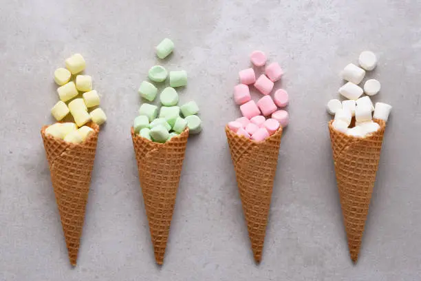 Four Sugar Waffle Ice Cream Cones filled with colorful marshmallows spilling onto tile table.