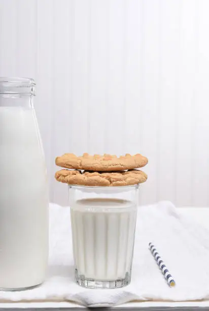 A Milk and Cookie Snack on a white table with white wall. Cookies are stacked on the glass of milk.