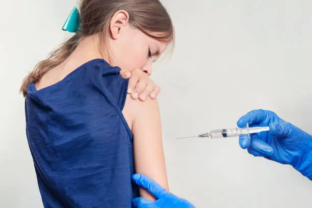 Photo of girl is vaccinated in her hands on a white background in the hospital. Routine vaccination against flu and colds. Prevention of the spread of coronavirus infection.