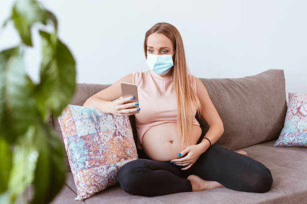istock Pregnant woman with a mask on her face is sitting on a sofa 1283260689