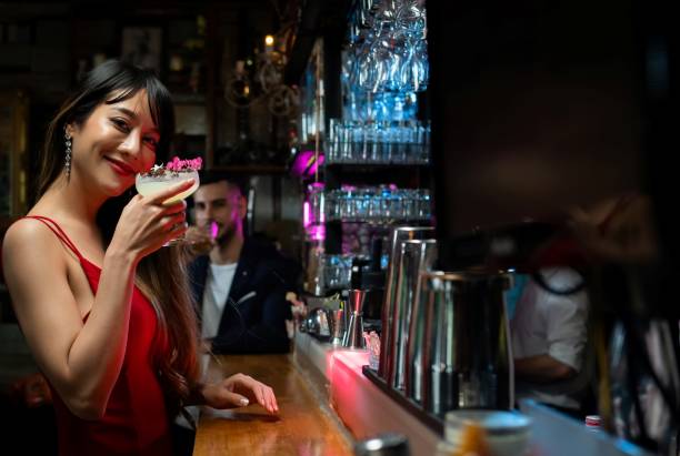 retrato de uma linda mulher asiática feliz em pé no balcão do bar segurando copo de coquetel e desfrutar de beber saboroso coquetel alcoólico de barman em boate. celebração da festa da vida noturna e conceito de feriado - home interior cocktail bar women - fotografias e filmes do acervo