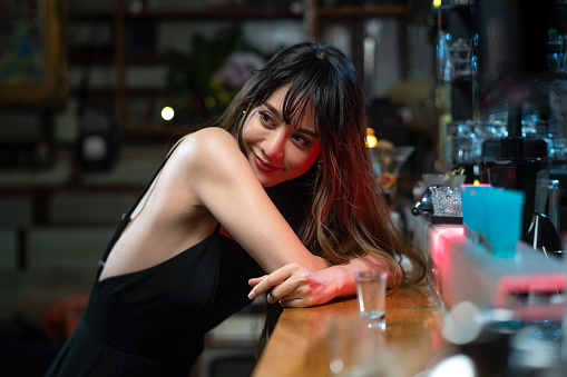 Portrait of Asian woman standing at bar counter enjoy drinking alcoholic drink in nightclub.