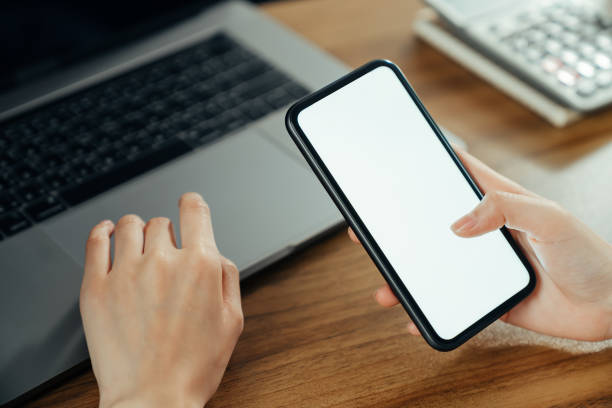 istock Woman hand holding smartphone with blank copy space screen for your advertisement. laptop on the table. 1283264302