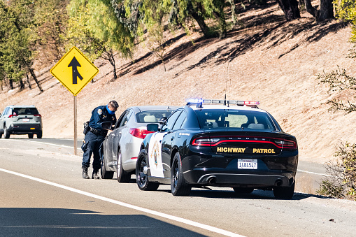 Oct 14, 2020 Fremont / CA / USA - Highway Patrol officer writing a traffic ticket to a driver pulled over on the right side of the road