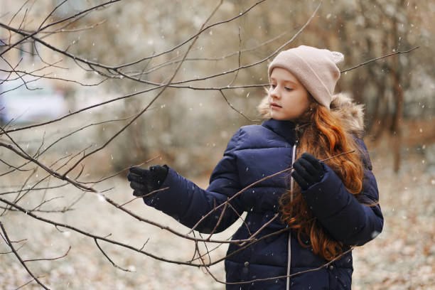menina bonita segurando um galho de árvore sem folhas em um fundo de flocos de neve caindo. - little girls autumn child red hair - fotografias e filmes do acervo