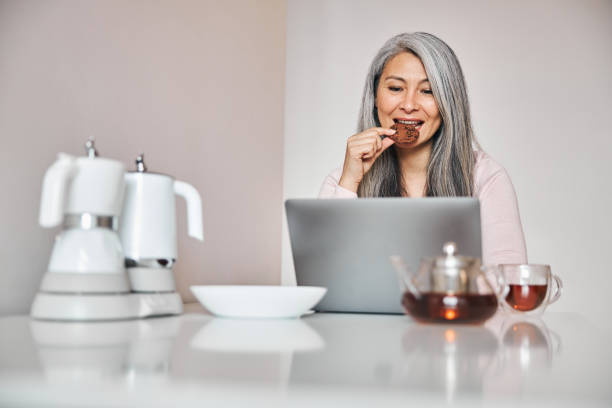 istock Beautiful woman using notebook and eating cookie at home 1283267850