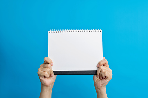 Human hand holding a blank spiral notebook.