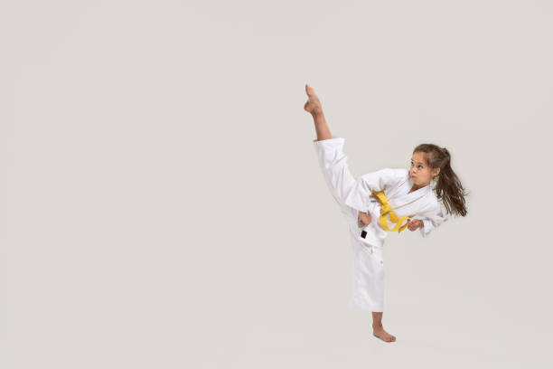 toma de longitud completa de la pequeña chica de karate en kimono blanco con una faja amarilla haciendo ejercicio y luchando, haciendo artes marciales, de pie aislado sobre fondo blanco - karate kicking tae kwon do martial fotografías e imágenes de stock