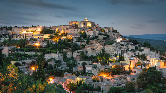 Gordes Medieval Village in French Provence under moody twilight dusk skyscape, Charming famous illuminated french village of Gordes built around and into mountain hill in french Provence Alpes Cote d'Azur, Gordes, Provence, South France, France, Europe