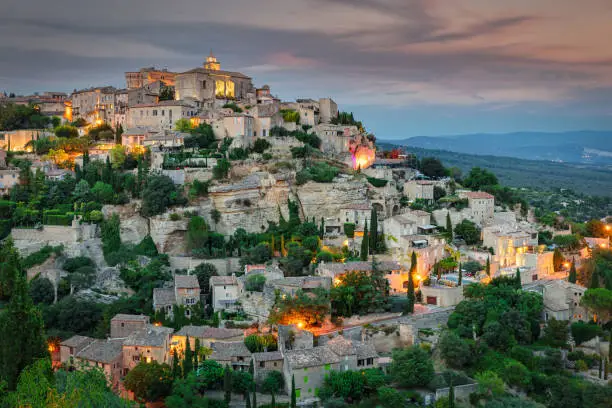 Gordes Medieval Village in French Provence under moody twilight dusk skyscape, Charming famous illuminated french village of Gordes built around and into mountain hill in french Provence Alpes Cote d'Azur, Gordes, Provence, South France, France, Europe