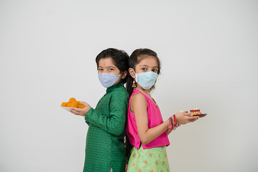 two kids in tradional dress in greeting pose wearing mask