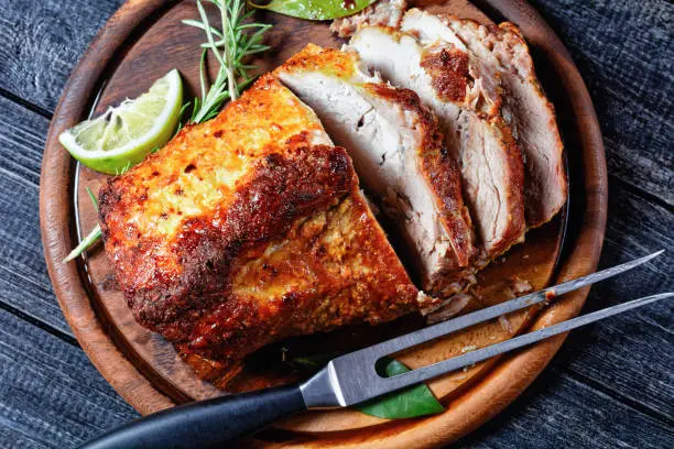 Sunday roasted pork tenderloin, juicy and succulent oven-baked piece of meat rubbed with mustard and spices: rosemary, bay leaf, lime juice, and pepper on a wooden background, close-up, top view