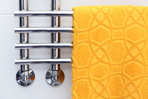 A yellow towel is dried on a heated towel rail.Heated Towel Rack. Polished Stainless Steel.Hotel Fabric. Wall style. Towel warmer for the bathroom.