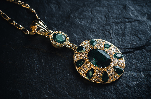 Gold pendant with green emeralds on a black stone background close up