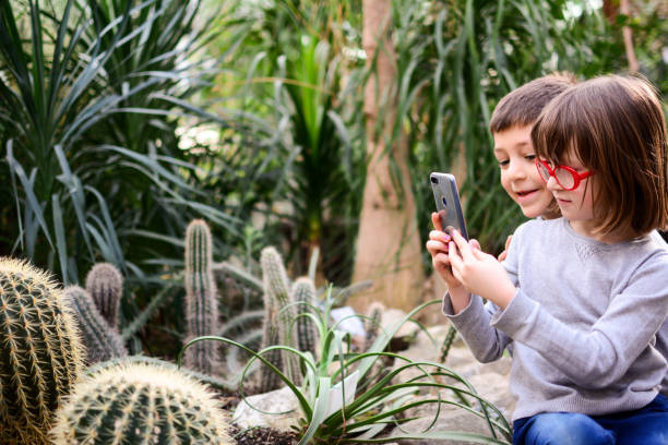 Playful brother and sister making faces while taking selfie in greenhouse.