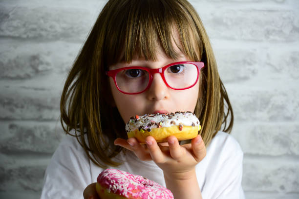 istock Young Girl Sitting At Table Eating Sugary Donut 1283304504