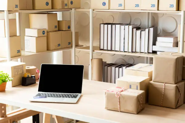 Photo of Parcel boxes on shelf and color shopping bags placing near laptop on table. SME business on shopping online at home office packaging on background is popular business.